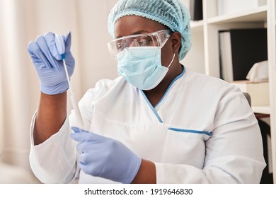 Portrait View Of The Confident Skilfull Multiracial Nurse Sitting At The Table And Holding Tube With Covid 19 PCR Test Before The Testing Patient At The Hospital. Stock Photo