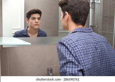 Portrait view of a young teenager man looking at himself in a home bathroom mirror, getting ready for school in the morning, home interior. Health and well being, male care and grooming, indoors.