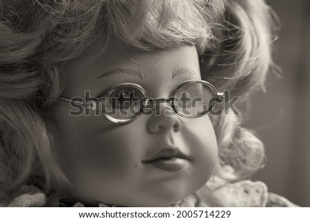 Portrait of a vintage baby doll, toy girl with blond hair and glasses.