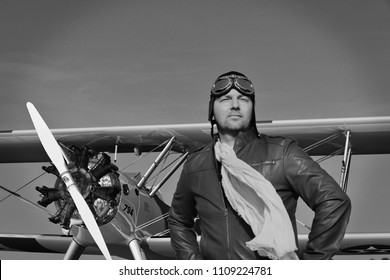 Portrait Of A Vintage Pilot With Leather Cap, Scarf And Aviator Glasses In Front Of A Historic Airplane Biplane - Portrait Of A Man In Historical Pilot Clothing - Vintage Old Picture Style