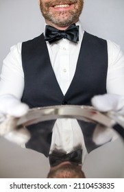 Portrait of Waiter or Butler in Black Vest and White Gloves Holding a Silver Serving Tray and Smiling Politely. Concept of Service Industry and Professional Courtesy.