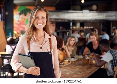 Portrait Of Waitress Holding Menus Serving In Busy Bar Restaurant