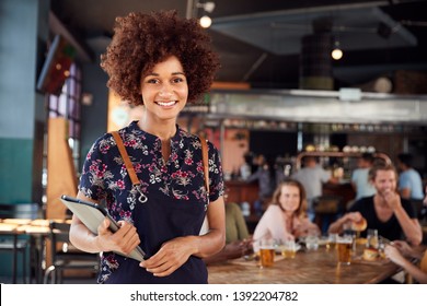 Portrait Of Waitress Holding Menus Serving In Busy Bar Restaurant