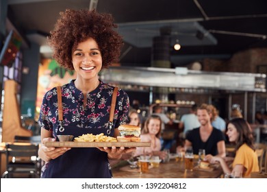 Portrait Of Waitress Serving Food To Customers In Busy Bar Restaurant - Powered by Shutterstock