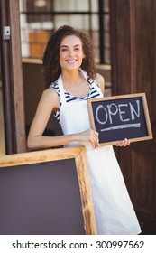 Portrait Of Waitress Showing Chalkboard With Open Sign At Coffee Shop