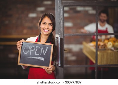 Portrait Of Waitress Showing Chalkboard With Open Sign At Coffee Shop