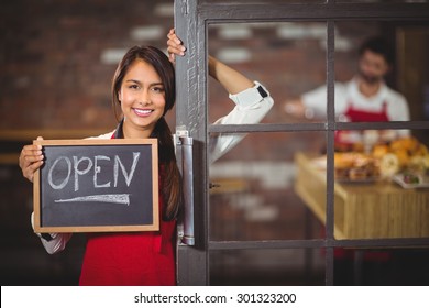 Portrait of waitress showing chalkboard with open sign at coffee shop - Powered by Shutterstock