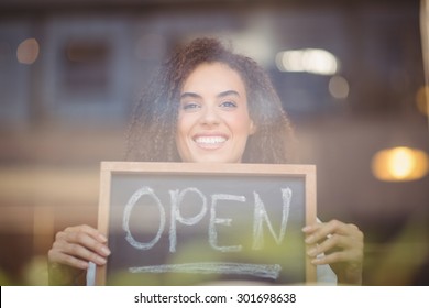 Portrait Of A Waitress Showing Chalkboard With Open Sign At The Coffee Shop