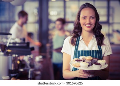 Portrait of a waitress showing a plate of cupcakes at the coffee shop - Powered by Shutterstock