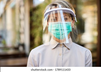 Portrait of waitress wearing visor and protective face mask while working at cafe during virus epidemic.
