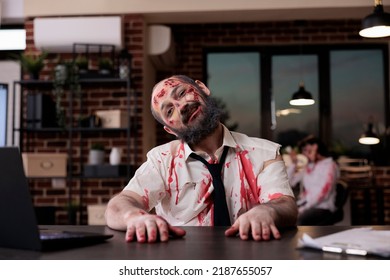 Portrait Of Walking Dead Corpse In Office Working On Startup Business With Laptop, Creepy Evil Monster Sitting At Desk. Brain Eating Horrific Zombie With Bloody Wounds And Dirty Scars, Eerie Walker.