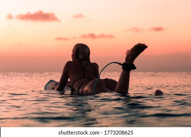 Portrait from the water of surfer girl with beautiful body on surfboard in the ocean at colourful sunset time in Bali