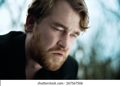 A portrait of a well dressed depressed man sitting on a bench in a park crying with a tear on his cheek.