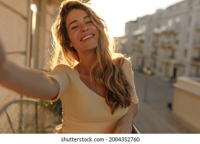 Portrait Of Well-groomed Woman With Gorgeous Smile With Teeth And Long Hair Against The Backdrop Of City. Takes Selfie While Standing On Her Summer Terrace.