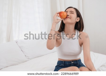 Portrait of white Asian woman with a tattoo sitting on the bed relaxing and playing laptop on weekend There was bread and fruit and red apples on a white bed to eat. holiday concept