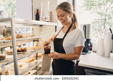 Portrait of white Caucasian beautiful barista woman taking muffin pastry from shop-window. Person at work place small business concept - Powered by Shutterstock