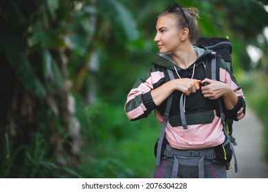 Portrait Of A White Caucasian Girl With A Hiking Backpack. Young Girl In A Spring Jacket And Clothes For Hiking On The Background Of The Jungle.