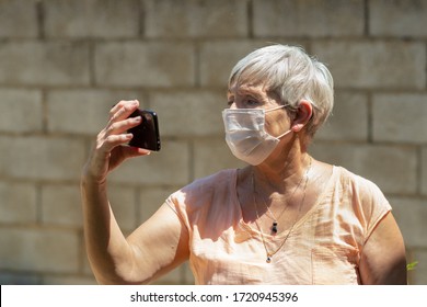 Portrait Of White Haired Older Caucasian Woman With Face Mask Removing A Photo