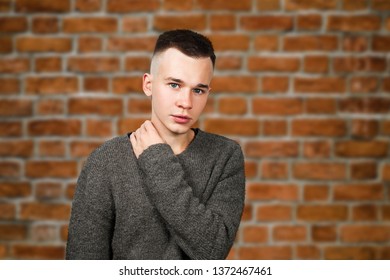 Portrait White Yong Guy In Gray Sweater And Short Haircut, On Brick Wall Background