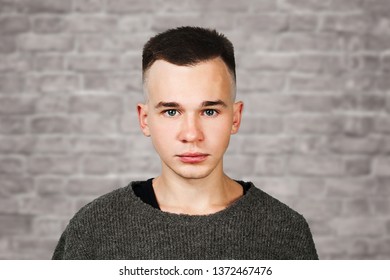 Portrait White Yong Guy In Gray Sweater And Short Haircut, On Brick Wall Background