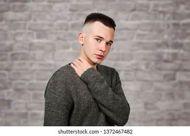 Portrait White Yong Guy In Gray Sweater And Short Haircut, On Brick Wall Background