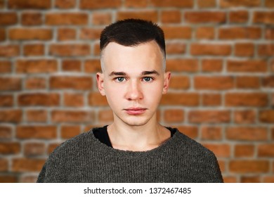 Portrait White Yong Guy In Gray Sweater And Short Haircut, On Brick Wall Background