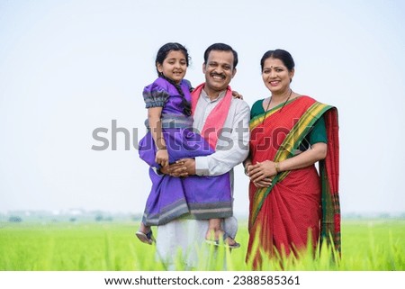 Portrait wide shot of Happy smiling Indian village farming couple with kid standing by looking at camera near paddy farmland - concept of relationship,family harmony and togetherness