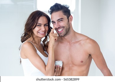 Portrait wife smiling while applying cream on husband face at home - Powered by Shutterstock