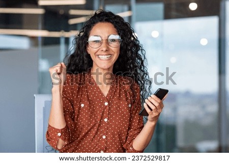 Portrait of winner woman, close-up businesswoman smiling and looking at camera celebrating triumph and elation, holding hand up gesture of achieving results, female worker inside office.