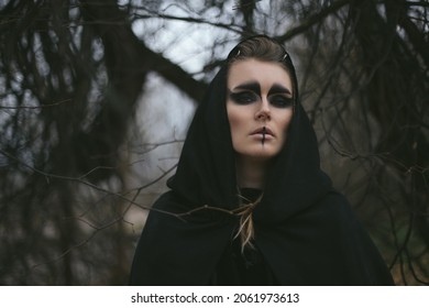 portrait of a witch in a hood and a cloak in the forest. Halloween mystical atmosphere. Celtic mythology goddess Valkyrie. Spiritualism spell rite. Masquerade makeup costume witch. Magic witchcraft
