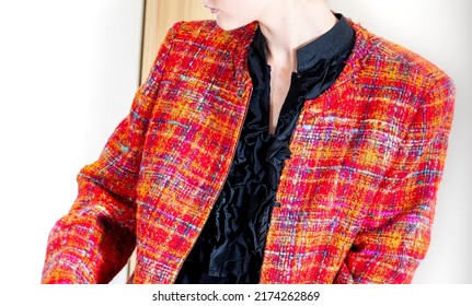 A portrait without a face of a beautiful young woman in black blouse trying on red jacquard chanel style jacket