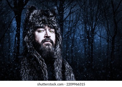 Portrait Of A Wolfman In The Night Forest With Snow Flakes. Adult Bearded Man In Winter Clothes. Cold Weather, Low Temperature, Snow And Frost. A Stern Man Is Not Afraid Of The Cold.