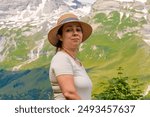 Portrait of a woman aged 40-45 wearing a straw hat against the background of snowy peaks of the Austrian Alps. Behind her, the mountains rise in the distance.