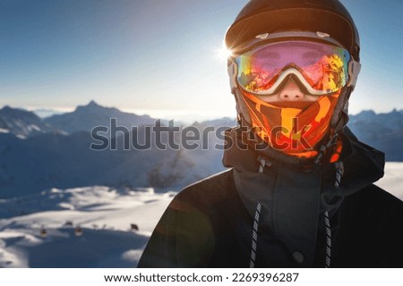 Portrait of a woman in the Alps. A young woman, a snowboarder or a skier in a snowy winter on a mountain slope, her beautiful happy eyes are visible through a ski mask or goggles