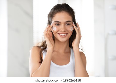 Portrait Of Woman Applying Face Cream On Cheeks Smiling To Camera, Moisturizing Caring For Skin In Bathroom At Home. Beauty Care Routine, Facial Skincare Concept - Powered by Shutterstock