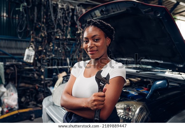 Portrait of woman auto mechanic working at car\
repair shop with looking at\
camera.