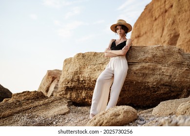 Portrait of woman in black bralette and white trousers leaning on rock at beach