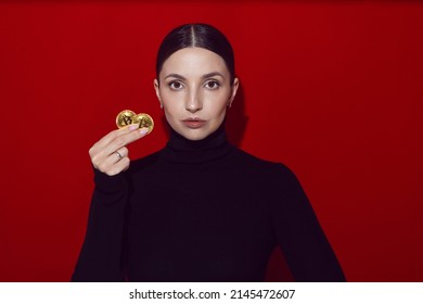 portrait of a woman in black clothes holding a gold bitcoin coin on a red background in the studio. Digital cryptocurrency bitcoin.