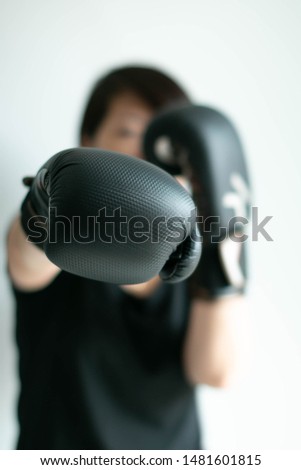 Portrait of woman in black T-shirt and black boxing gloves stretching her right fist forward; right jab; sport and health care; selected focus at tip of the fist. Concept of aim in business. 