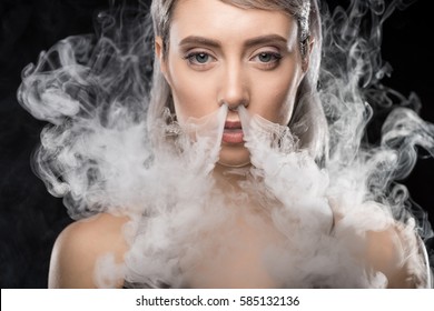 portrait of woman in bodysuit exhaling smoke isolated on black
