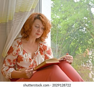 Portrait of a woman with a book in her hands sitting on a windowsill