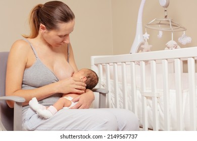 Portrait of woman breastfeed newborn infant baby sitting on the chair near the crib