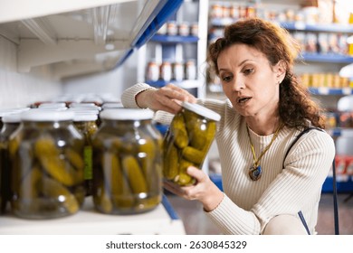 Retrato de la mujer que compra los pepinos enlatados en la tienda de comestibles
