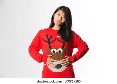 Portrait of woman in Christmas sweater showing she has eaten too much food over gray background