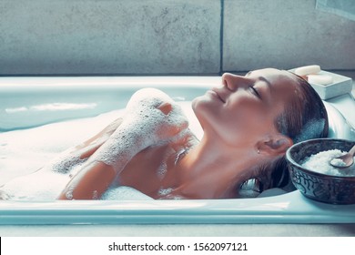 Retrato de uma mulher com os olhos fechados de prazer tomando banho em casa, mulher com prazer gosta de banho com espuma, um dia no spa, conceito de higiene e relaxamento