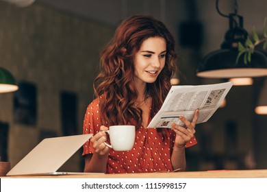 portrait of woman with cup of coffee reading newspaper at table with laptop in cafe - Powered by Shutterstock