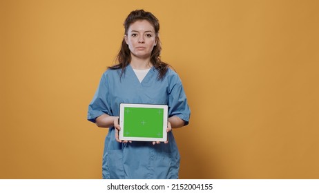 Portrait Of Woman Doctor Holding Tablet Computer With Green Screen Wearing Hospital Uniform For Health Care Concept In Studio. Medic Using Digital Touchscreen Device For Advertising Copy Space.