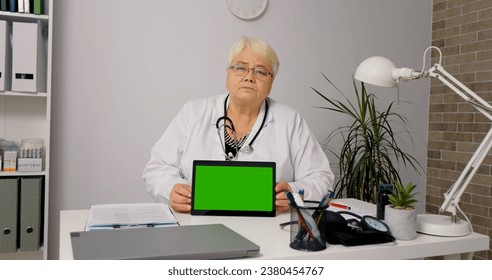 Portrait of woman doctor holding tablet with green screen wearing hospital uniform for health care concept in studio. Medic using digital touchscreen device for advertising copy space. - Powered by Shutterstock