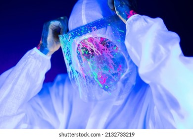 Portrait Of Woman Doctor In Protective Clothes In Ultraviolet Neon Light During Coronavirus Pandemic. Epidemic, Pandemic Of Coronavirus Covid-19. Doctor, Patient In Respirator.