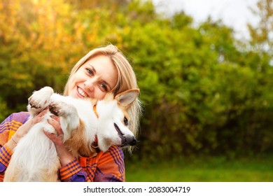 Portrait of a woman with a dog corgi breed. A beautiful blonde woman hugs her beloved pet, closing her eyes. Natural autumn background. The concept of an active lifestyle with a pet.